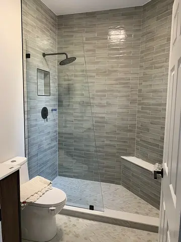 A shower with gray tiles and a frameless glass splash panel cut at an angle and installed by Glass Doctor of Nashville.